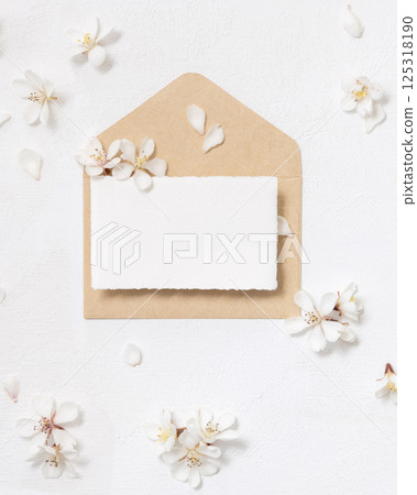Blank paper card over envelope near white cherry flowers top view, spring wedding mockup 125318190