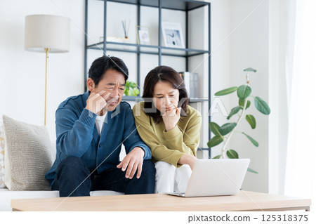A middle-aged couple using a computer in the living room A middle-aged couple using a computer in the living room 125318375