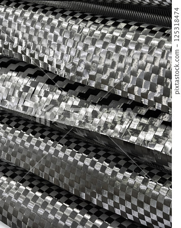 Textured carbon fiber materials stacked in layers showcasing intricate woven patterns and shine under studio lighting 125318474