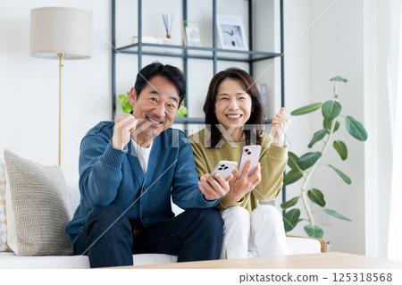 一對中年夫婦，在客廳裡看著智能手機 125318568