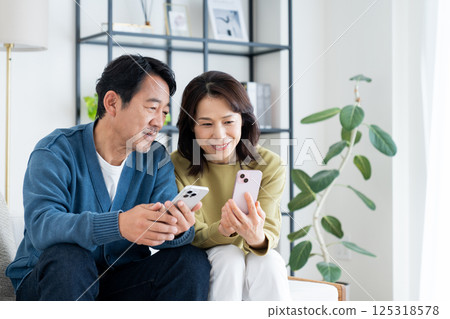 A middle-aged couple watching a smartphone in the living room A middle-aged couple watching a smartphone in the living room 125318578