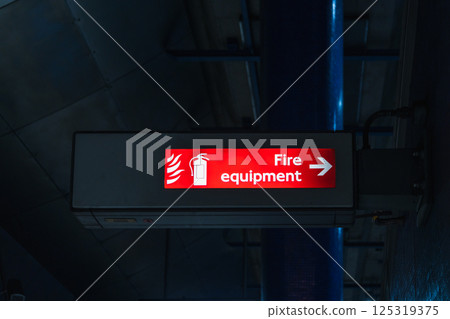 Illuminated Fire Equipment Sign with Arrow in Dark Indoor Industrial Setting Illuminated Fire Equipment Sign with Arrow in Dark Indoor Industrial Setting 125319375