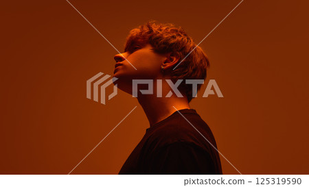 Side view of young man with tilted head with expression unreadable in soft orange haze against bright gradient background. Concept of beauty 125319590