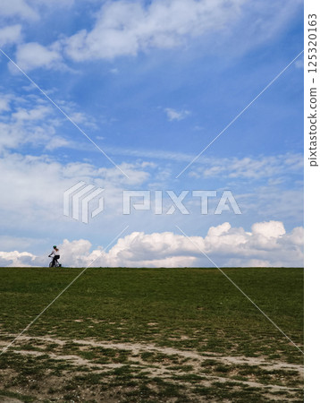 Cyclist enjoying a leisurely ride on a green hill under a beautiful cloudy sky, embracing the freedom of the open road 125320163