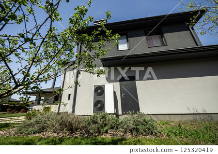 Eco-efficient air source heat pump installed on wall of modern house with green garden in spring setting Eco-efficient air source heat pump installed on wall of modern house with green garden in spring setting 125320419