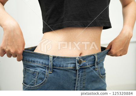 Young Asian woman losing weight wearing loose pants in oversize jeans. 125320884