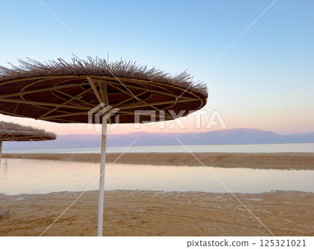 Parasol straw umbrella near sea shore. Straw umbrellas on hot summer day by beach. Sunny blue skies warm weather enjoyed on beach under parasol made of straw. Vacation in tropical countries 125321021