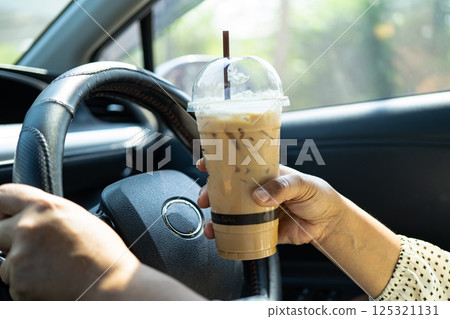 Asian woman driver hold ice coffee cup for drink in car, dangerous and risk an accident. 125321131