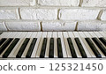 鍵盤的白鍵和黑鍵放置在白色磚塊狀瓷磚牆前 125321450