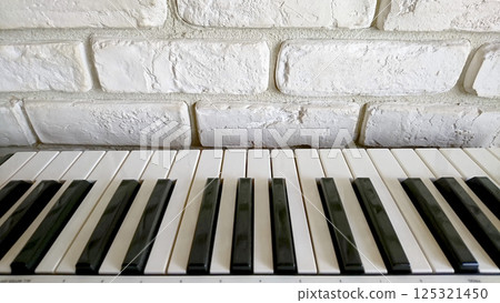 鍵盤的白鍵和黑鍵放置在白色磚塊狀瓷磚牆前 鍵盤的白鍵和黑鍵放置在白色磚塊狀瓷磚牆前 125321450