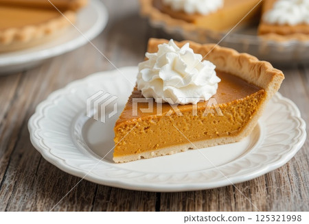 Slice of pumpkin pie crowned with whipped cream, placed on white plate. Slice of pumpkin pie crowned with whipped cream, placed on white plate. 125321998