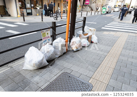 Burnable garbage dumped on the sidewalk; household garbage placed in white bags 125324035
