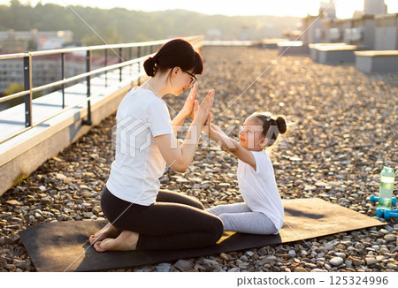 Mother and young daughter participating in outdoor exercise. Shows a bonding activity enhancing fitness, coordination, and emotional connection. Illustrates warmth, unity and healthy family lifestyle. Mother and young daughter participating in outdoor exercise. Shows a bonding activity enhancing fitness, coordination, and emotional connection. Illustrates warmth, unity and healthy family lifestyle. 125324996