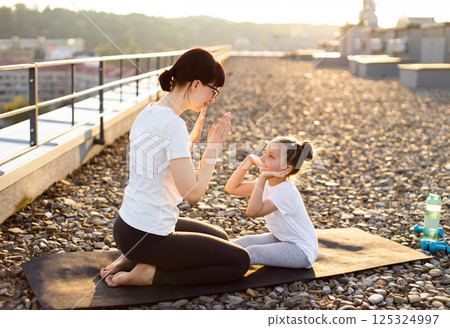 Mom and daughter doing fitness exercises on rooftop during sunset, sharing bonding moment. Woman teaching young girl workout techniques. Inspirational scene highlights positive energy, health Mom and daughter doing fitness exercises on rooftop during sunset, sharing bonding moment. Woman teaching young girl workout techniques. Inspirational scene highlights positive energy, health 125324997