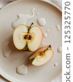 sliced green apple in drops of water on a white plate 125325770