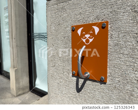Dog leash hook installed outdoors for pet owners to secure their dogs safely. Happy dog face icon adds friendly touch, promoting responsible pet ownership in modern urban areas 125326343
