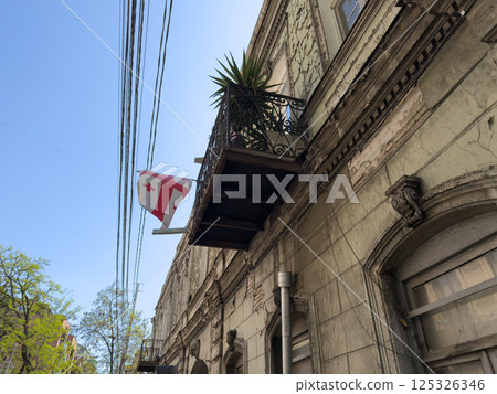 Street view featuring worn down architecture and balcony with potted plant. Power lines stretch across clear sky, capturing real urban life and mood in an older district of Tbilisi, Georgia Street view featuring worn down architecture and balcony with potted plant. Power lines stretch across clear sky, capturing real urban life and mood in an older district of Tbilisi, Georgia 125326346