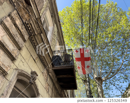 Aged building with cracked walls, cast iron balcony, and symbolic flag of Georgia evoke nostalgic mood. Warm textures and historic character highlight authentic city life under soft natural light 125326349