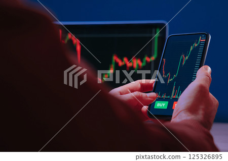 trader holding smartphone, using trading app for analyzing stock market 125326895