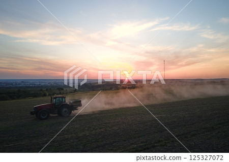 Tractor spraying fertilizers with insecticide herbicide chemicals on agricultural field at sunset Tractor spraying fertilizers with insecticide herbicide chemicals on agricultural field at sunset 125327072