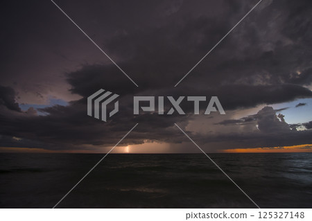Sunset landscape of dark ominous rainstorm with lightning and thunder over sea water waves. Beautiful seascape in evening 125327148