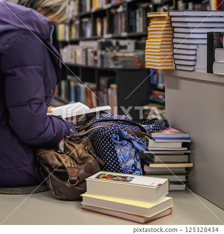 Woman sitting in bookstore reading a book among piles of literature. Scene reflects peaceful moment, passion for reading and immersive book discovery Woman sitting in bookstore reading a book among piles of literature. Scene reflects peaceful moment, passion for reading and immersive book discovery 125328434
