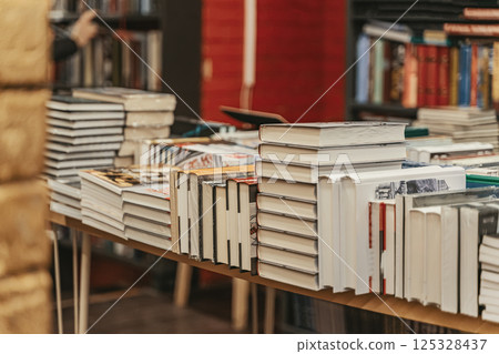 Stacks of hardcover books displayed on bookstore tables during busy literary season. Bookstore atmosphere evokes passion, curiosity and timeless love for books Stacks of hardcover books displayed on bookstore tables during busy literary season. Bookstore atmosphere evokes passion, curiosity and timeless love for books 125328437