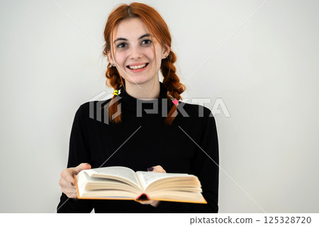 Portrait of young smiling student girl with an open book in her hands. Reading and education concept. 125328720