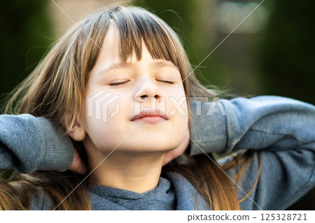 Portrait of young pretty child girl with long hair enjoying warm sunny day in summer outdoors. Cute female kid relaxing on fresh air outside. 125328721