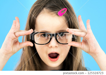 Portrait of surprised child girl wearing looking glasses holding hands to her face isolated on blue background. 125328723