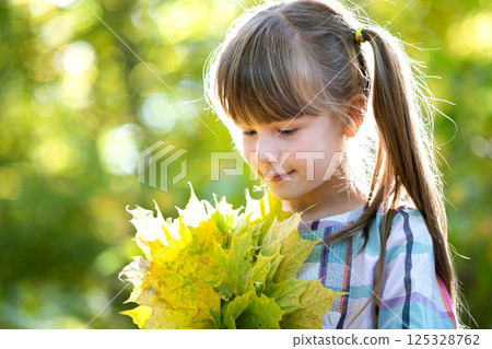 Portrait of happy pretty child girl holding a bunch of fallen tree leaves in autumn forest. Positive female kid enjoying warm day in fall park. Portrait of happy pretty child girl holding a bunch of fallen tree leaves in autumn forest. Positive female kid enjoying warm day in fall park. 125328762