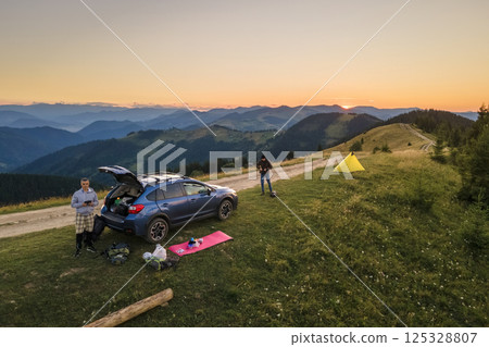 Offroad camping site on hillside at bright sunset. SUV vehicle and tent shelters on mountain campsite on sunny evening. Active tourism and hiking concept 125328807