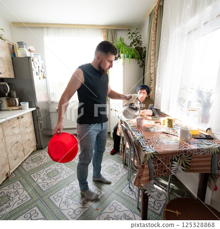 Engaging moments in a cozy kitchen as a man prepares food while a woman enjoys a quiet moment surrounded by sunlight and plants 125328868