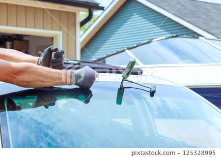 Skilled technician worker is replacing damaged windshield on vehicle, ensuring precise replacement windshield 125328995
