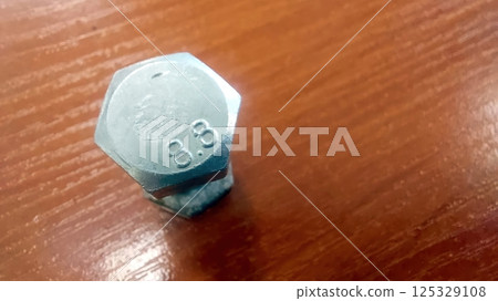 Hexagonal bolt resting on a wooden table displays detailed markings and reflections 125329108