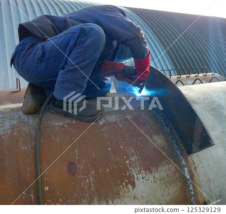 Welder performing a pipe welding task in an industrial setting during daylight hours Welder performing a pipe welding task in an industrial setting during daylight hours 125329129