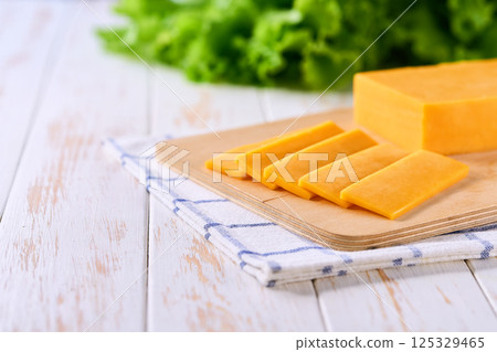 pieces of yellow cheddar cheese on a white wooden table, copy space for text. 125329465