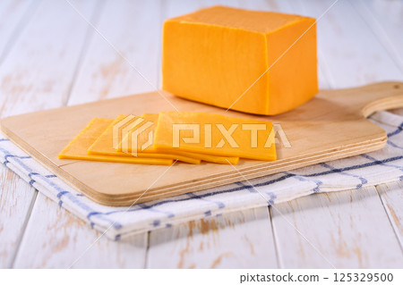 Slices of cheddar cheese on a cutting board, selective focus. 125329500