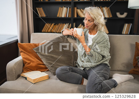 Good morning autumn winter fall vibe. Comfort relaxed senior old elderly woman drinking hot beverage tea coffee in sofa at home. Mature woman resting enjoy calm morning at home alone. Pension concept 125329628