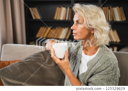 Good morning autumn winter fall vibe. Comfort relaxed senior old elderly woman drinking hot beverage tea coffee in sofa at home. Mature woman resting enjoy calm morning at home alone. Pension concept Good morning autumn winter fall vibe. Comfort relaxed senior old elderly woman drinking hot beverage tea coffee in sofa at home. Mature woman resting enjoy calm morning at home alone. Pension concept 125329629