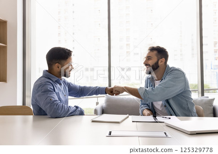 Smiling motivated young male teammates exchange fist bump at workplace 125329778
