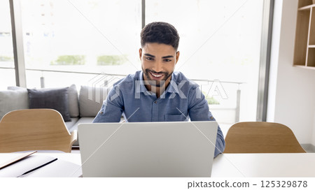 Happy gen z male employee using notebook at comfortable workplace 125329878