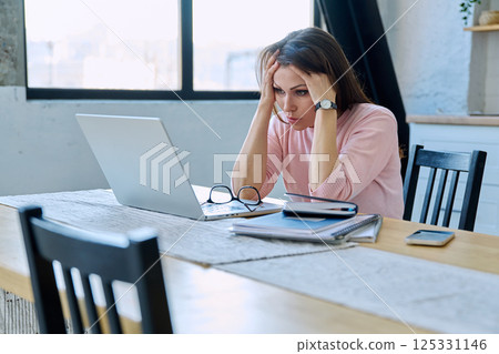 Middle aged sad stressed woman sitting at home at table with computer Middle aged sad stressed woman sitting at home at table with computer 125331146