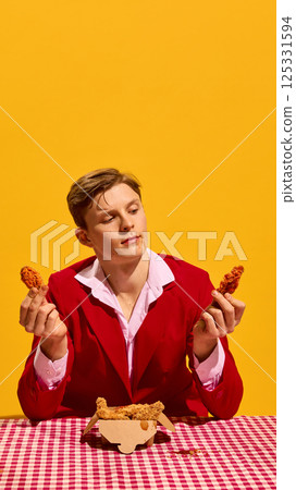 Man holding two chicken nuggets pieces comparing them in serious pose against yellow background. Man holding two chicken nuggets pieces comparing them in serious pose against yellow background. 125331594