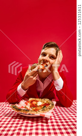 Man in red suit resting face on hand while eating pizza slice at checkered table with dreamy gaze on red background. Man in red suit resting face on hand while eating pizza slice at checkered table with dreamy gaze on red background. 125331611