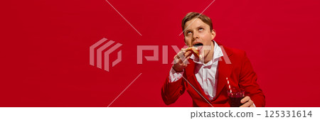 Man in red suit holding soda and dramatically biting pizza slice with ecstatic expression against bold red background. 125331614