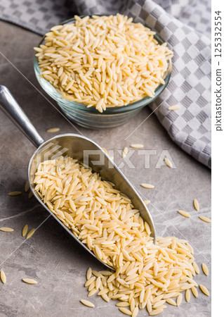 Orzo, kritharaki, risoni pasta. Uncooked dry pasta in scoop on kitchen table. 125332554