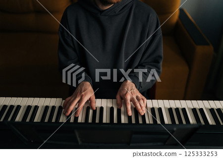 Cropped shot of male composer playing on eclectic piano at home studio. Closeup of talented musician creating beautiful melodic composition using synthesizer. Concept of recording music at home 125333253