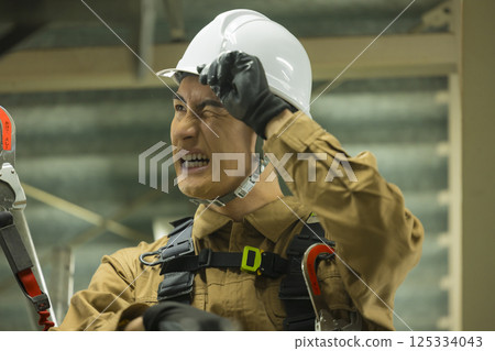 A male worker wearing a full harness climbing scaffolding 125334043