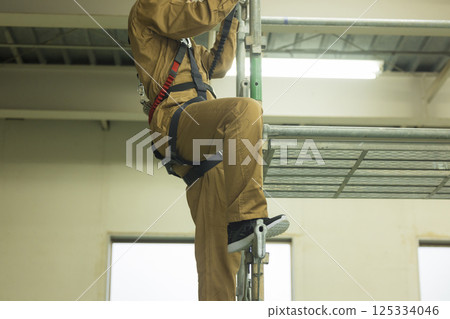 一名身穿全套安全帶的男工人攀爬鷹架 一名身穿全套安全帶的男工人攀爬鷹架 125334046